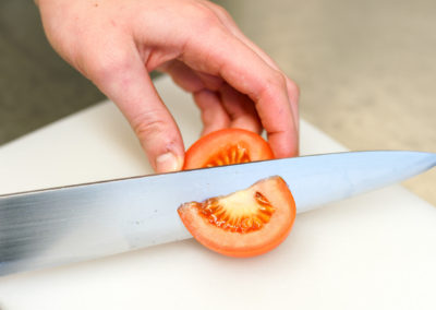 Tomate wird auf Brett von Messer aufgeschnitten
